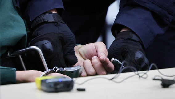 Ein Justizbeamter öffnet die Handschnellen des Angeklagten Ibrahim A. im Gerichtssaal. © dpa Foto: Christian Charisius