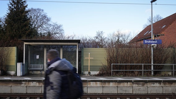 Ein Kreuz mit den Namen der Opfer der Messerattacke ist neben dem Wartehäuschen des Bahnhofs in Brokstedt aufgestellt. © dpa Foto: Christian Charisius