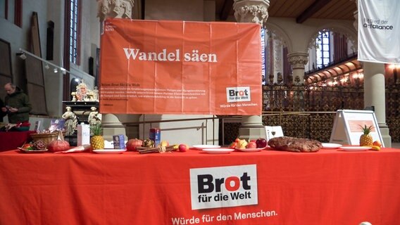 Früchten und Brot stehen auf einem mit einer orangen Decke gedeckten Tisch im St. Petri Dom in Schleswig bei einer Aktion von Brot für die Welt. © NDR 