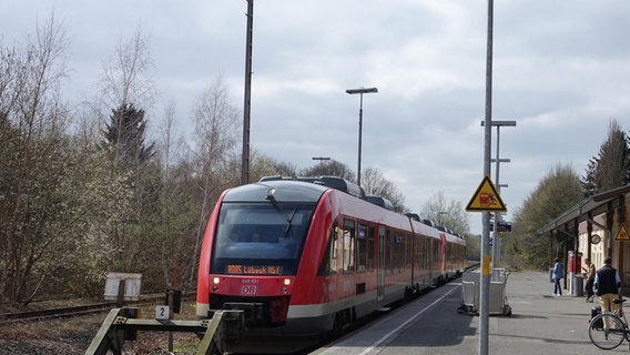 Ein roter Regionalzug steht mit Ziel Lübeck HBF am Gleis. Drei Menschen befinden sich am Bahnsteig. © Daniel Friederichs Foto: Daniel Friederichs