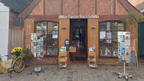 Eine urige Buchhandlung mit Kartenaussteller und gelbem Fahrrad vor dem Eingang. © NDR Foto: Laura Albus