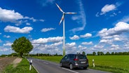 Ein Auto fährt unter blauem Himmel an einem Windrad vorbei. © picture alliance Foto: Jochen Tack