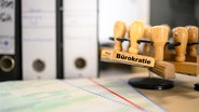 Ein Stempel mot der Aufschrift Bürokratie hängt an einem Stempelhalter. © imago images / Lobeca 
