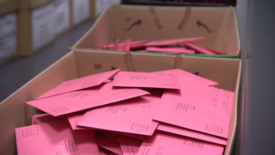 Viele Umschläge in Farbe rosa liegen in Kartons in einem Raum des Amts Kellinghusen. © NDR 