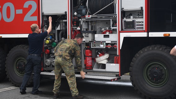Zwei Feuerwehrleute der Bundeswehr kontrollieren ihre im Löschfahrzeug befindliche Ausrüstung. © NDR Foto: Jörn Zahlmann