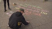 Frieda Müller schreibt mit bunter Kreide Sätze auf die Straße. © NDR Foto: NDR
