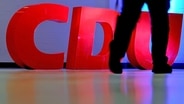 Ein Parteimitglied geht an dem CDU-Logo vorbei © picture alliance / dpa Foto: Angelika Warmuth