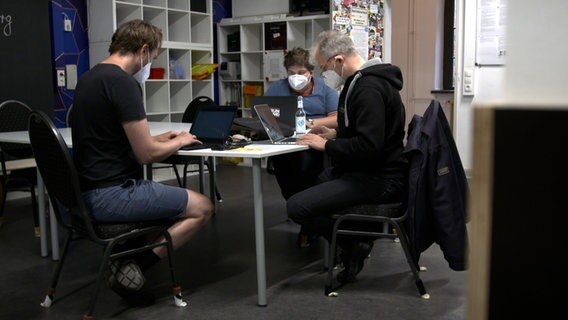 Drie leden van de Chaos Computer Club zitten met laptops aan een tafel.  © NDR 