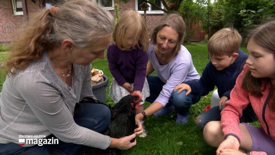 Zwei Frauen und drei Kinder blicken auf ein Huhn. © NDR 
