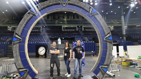 Zwie Männer und eine Frau posieren vor dem Stargate auf einer Convention. © NDR Foto: Martina Heller