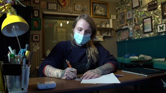 A tattoo artist sits at her workplace. © NDR