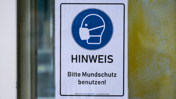 Ein Warnschild mit dem Hinweis "Bitte Mundschutz benutzen!" hängt an einer Scheibe. © imago images/Michael Gstettenbauer Foto: Michael Gstettenbauer