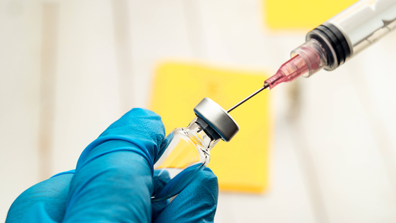 Ein Arzt zieht eine Spritze mit einem Impfstoff aus einer Ampulle auf. © imago images/Bihlmayerfotografie 