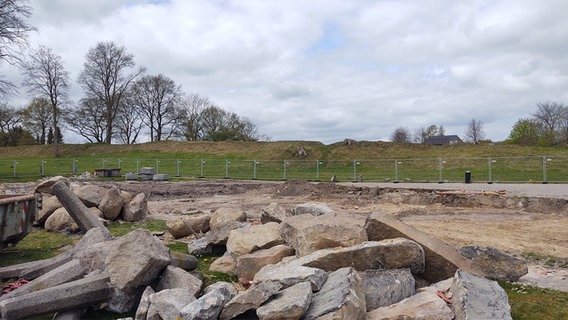 Feldsteine liegen auf einem Haufen mit einem Bauzaun im Hintergrund. Dahinter ist das Danewerk als grüner Wall zu sehen. © Peer-Axel Kroeske Foto: Peer-Axel Kroeske