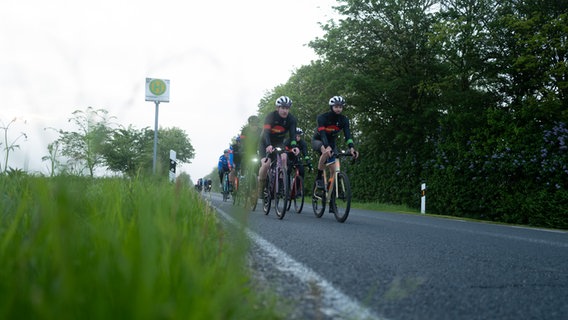Fahrradfahrerinnen und -fahrer fahren an einer Landstraße. © NDR Foto: Lisa Pandelaki