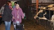 Eine alte Frau geht mit einem Rollator durch einen Kuhstall.  Foto: Claudio Campagna