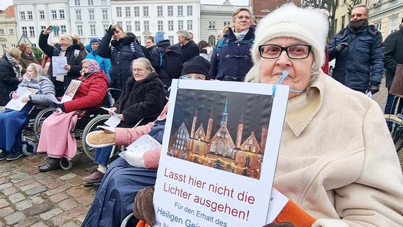 Eine im Rollstuhl sitzende Demonstrantin hält ein Plakat während einer Kundgebung für den Erhalt des Heiligen-Geist-Hospitals in die Kamera © NDR Foto: Julian Marxen