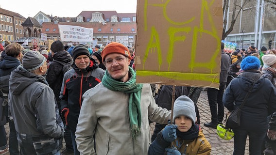 Ein Junge steht neben einem Mann und hält ein Plakat mit dem Schriftzug FCK AFD in seinen Händen bei einer Demonstration in Lübeck auf dem Rathausplatz gegen Rechtsextremismus. © NDR Foto: Phillip Kamke