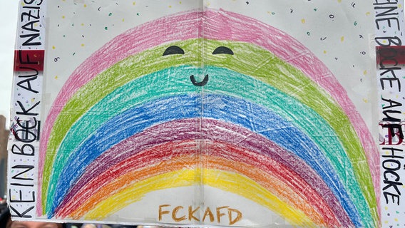 Ein Regenbogen mit lächelnden Augen und Mund und Schriftzug "FCK AFD" wird bei einer Demo gegen Rechtsextremismus in Henstedt-Ulzburg hochgehalten. © NDR Foto: Verena Sens