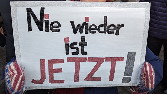 Eine Frau hält bei einer Demonstration gegen Rechtsextremismus auf dem Lübecker Rathausplatz ein Plakat mit dem Schriftzug "Nie wieder ist jetzt" in ihren Händen. Eine Frau hält bei einer Demonstration gegen Rechtsextremismus auf dem Lübecker Rathausplatz ein Plakat mit dem Schriftzug "Nie wieder ist jetzt" in ihren Händen. © NDR Foto: Phillip Kamke