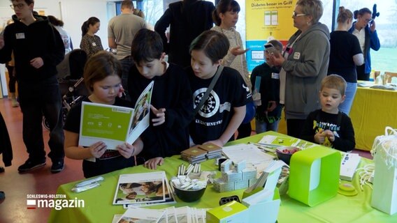 Kinder lesen Broschüren bei einer Selbsthilfe-Veranstaltung. © NDR 