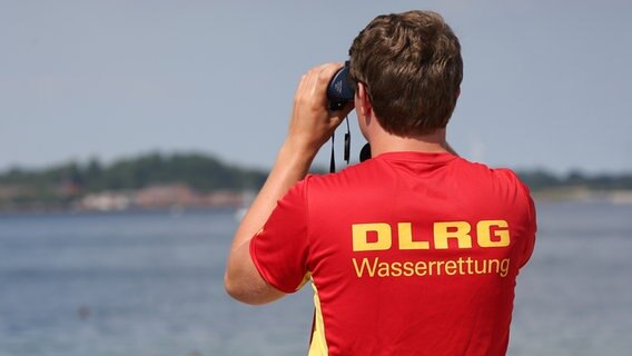 Eckernförde: Ein Rettungsschwimmer der Deutschen Lebensrettungsgesellschaft (DLRG), beobachtet das Geschehen am Strand. © picture alliance/dpa Foto: Bodo Marks