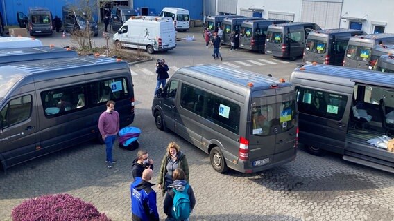 Auf einem Parkplatz stehen Menschen um zahlreiche Transporter herum.  Foto: Rafael Czajkowski