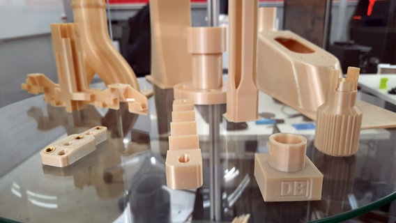 Verschiedene mit einem 3D-Drucker erstellten Kleinteile liegen auf einer Glasscheibe in einem Raum. © NDR Foto: Lina Bande