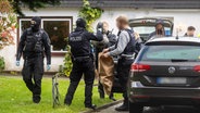 Polizisten beschlagnahmen einen Beutel auf einem Grundstück im Rahmen einer Drogendurchsuchung. © noltemedia Foto: Benjamin Nolte