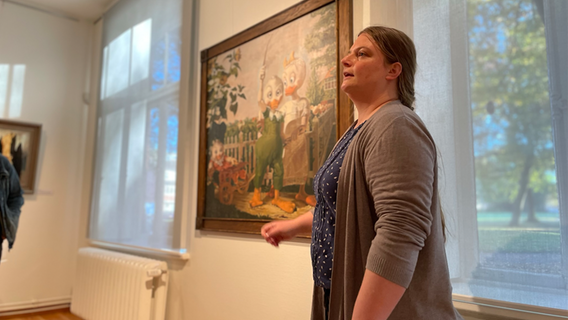 Eine Frau steht neben einem berühmten Werk, das im Stil von Donald Duck nachempfunden und im Rahmen der Wanderausstellung Duckomenta in Museum und Stiftung Landdrostei in Pinneberg ausgestellt ist. © NDR Foto: Jonas Hanst