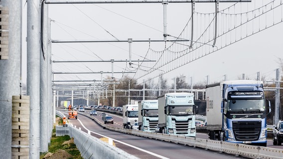 Lastwagen fahren auf der Autobahn 1 bei Reinfeld an neu installierten Oberleitungssystemen vorbei. In Schleswig-Holstein lässt die Freigabe der Teststrecke weiter auf sich warten. © dpa-Bildfunk Foto: Markus Scholz