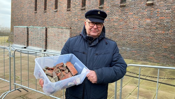 Ein Mann hält eine Kiste Pflastersteine in die Kamera. Ein Mann hält eine Kiste Pflastersteine in die Kamera. © NDR Foto: Karen Jahn