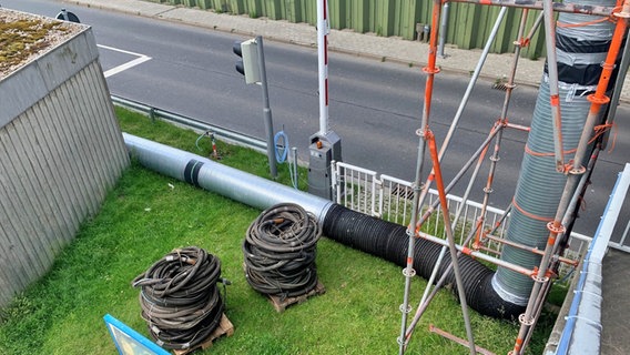 Von einer Brücke führen temporär Rohre herunter. Verschiedene Schläuche liegen auf Paletten. © NDR Foto: Jonas Salto