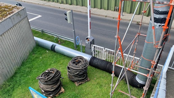 Von einer Brücke führen temporär Rohre herunter. Verschiedene Schläuche liegen auf Paletten. © NDR Foto: Jonas Salto