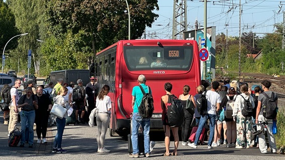 Bahnreisende stehen hinter einem roten Bus in Elmshorn. Bahnreisende stehen hinter einem roten Bus in Elmshorn. © NDR Foto: Samir Chawki