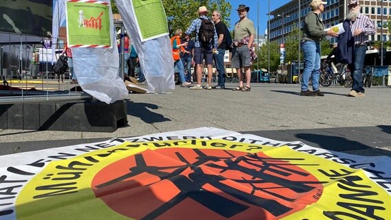 Im Vordergrund liegt ein Banner mit einem Schriftzug, im Hintergrund stehen mehrere Demonstrierende. Im Vordergrund liegt ein Banner mit einem Schriftzug, im Hintergrund stehen mehrere Demonstrierende. © NDR Foto: Fabian Boerger