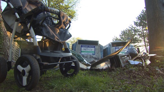 Ein Kinderwagen und illegal entsorgter Müll stehen vor zwei silbernen Müllcontainern. © NDR 