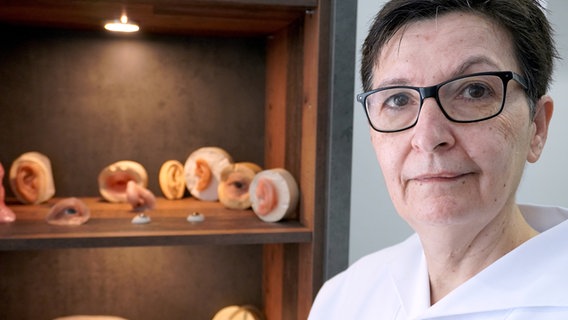 Eine Frau steht vor mehreren Silikon Epithesen. © NDR Foto: NDR