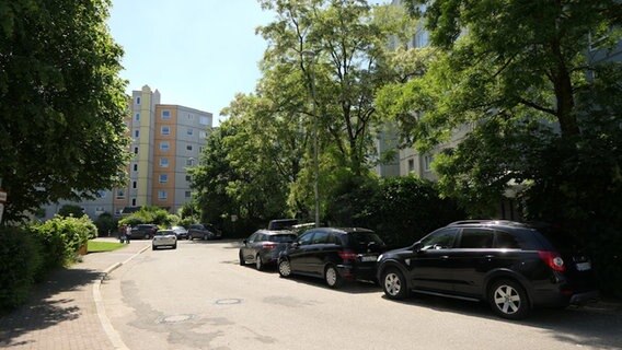 Eine Straße mit Blick auf Hochhäuser, umgeben von Bäumen. Autos parken an der Seite. © Daniel Friederichs Foto: Daniel Friederichs