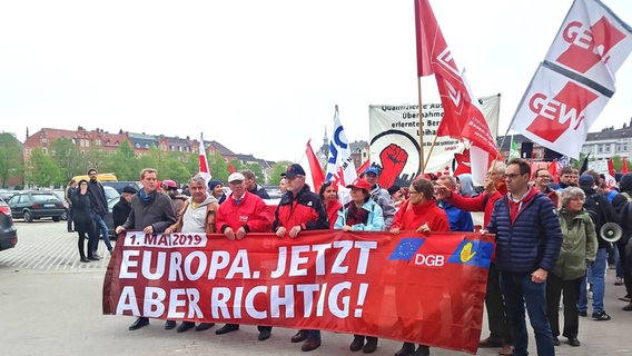 Menschen demonstrieren auf einem großen Platz und halten Fahner und Banner hoch. © NDR Foto: Keven Bieler