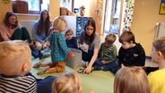 Die Auszubildende Lea Raddatz sitzt mit Kindern der Kita in einem Sitzkreis und spielt zusammen mit diesen. © Johannes Tran Foto: Johannes Tran