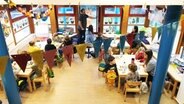 Ein Raum in einer Kindertagesstätte mit vielen Kindern und drei Erziehern, die an vier Tischen sitzen. © Johannes Tran Foto: Johannes Tran
