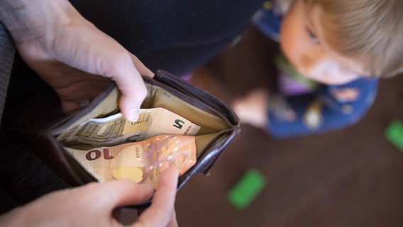 In einem geöffneten Potemonnaie ligene zwei Geldscheine, im Hintergrund ist ein Kind. © Imago Images | photothek Foto: photothek