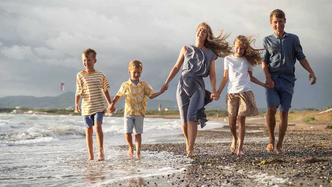 Eine Familie spaziert lächelnd einen Strand entlang.