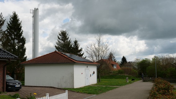 Das Blockheizkraftwerk am Birkenweg in Süderbrarup: Ein Firmengebäude in etwa der Größe eines Hauses, dahinter ein Schornstein.  © NDR Foto: Peer-Axel Kroeske