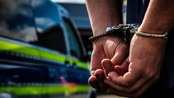 Zwei Hände in Handschellen vor einem Polizeiwagen. © Fotostand Foto: K. Schmitt