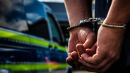Zwei Hände in Handschellen vor einem Polizeiwagen © Fotostand Foto: K. Schmitt