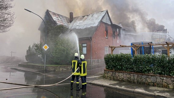 Zwei Einsatzkräfte der Feuerwehr löschen mit einem Feuerwehrschlauch ein Haus in Wohlde. © Benjamin Nolte Foto: Benjamin Nolte
