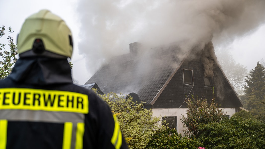 Eine Einsatzkraft der Feuerwehr steht vor einem brennenden Haus