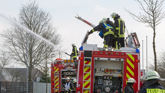 Feuerwehrmänner stehen auf einem Feuerwehrfahrzeug und löschen einen Brand. © noltemedia Foto: Benjamin Nolte